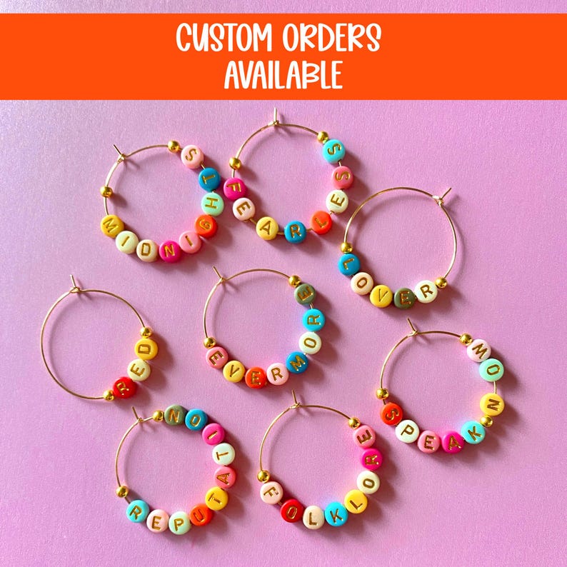 May include: Gold hoop earrings with colorful letter beads spelling out words like "MIDNIGHT", "SPEAK", and "FOREVER". The image also includes the text "CUSTOM ORDERS AVAILABLE" in white letters on an orange background.