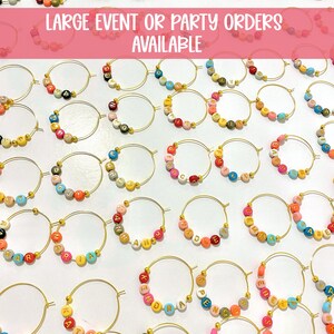 May include: A collection of gold hoop earrings, each adorned with colorful letter beads spelling out various names and words. The earrings are arranged on a white surface, with the text "LARGE EVENT OR PARTY ORDERS AVAILABLE" at the top.