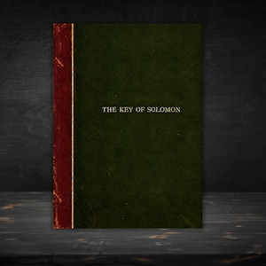 May include: A hardcover book with a dark green cover and a deep red spine. The title THE KEY OF SOLOMON is printed in gold lettering on the front cover. The book features a vertical gold line separating the red spine from the green cover.