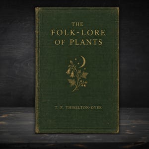 Puede incluir: Un libro de tapa dura de color verde oscuro titulado The Folk-Lore of Plants de T. F. Thiselton-Dyer. La portada presenta texto en relieve dorado y una ilustración central de una planta con flores bajo una luna creciente y estrellas.