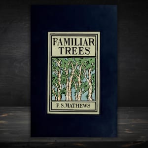 May include: A hardcover book titled Familiar Trees by F.S. Mathews with a dark blue cover. The central rectangular illustration features a light green and blue forest scene with white tree trunks and black outlines, framed by a cream border.