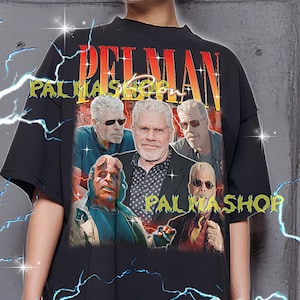 Puede incluir: Camiseta negra con un estampado de varias personas y los textos "PALMAN" y "PALMASHOP" en rojo y amarillo. La camiseta tiene cuello redondo y mangas cortas. La modelo lleva una camiseta XL.