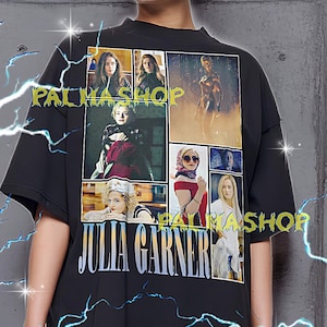 以下が含まれることがあります： 黒色のオーバーサイズTシャツ。コラージュ画像と白抜きの「JULIA GARNER」の文字がプリントされています。Tシャツには緑色の「PALMASHOP」の文字も。モデルはXLサイズのシャツを着用しています。