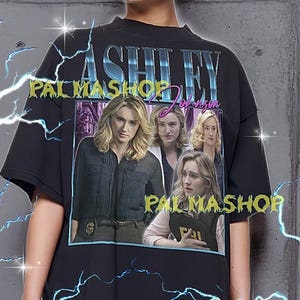 Puede incluir: Camiseta negra de gran tamaño con un gráfico de Ashley Johnson y el texto "ASHLEY JOHNSON PALMASHOP". La camiseta tiene cuello redondo y mangas cortas. La modelo lleva una camiseta XL. La camiseta es fiel a la talla.