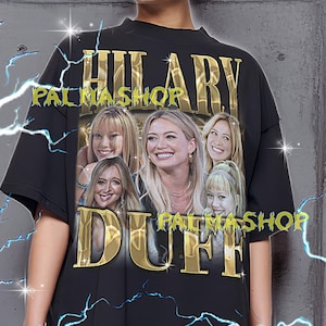Könnte beinhalten: Schwarzes T-Shirt mit einem goldenen Design, das den Text "HILARY DUFF PALMASHOP" und eine Collage von Bildern zeigt. Das T-Shirt wird von einer Person getragen. Das T-Shirt ist ein Unisex-Stil.