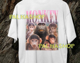 Op de afbeelding: Wit t-shirt met een afbeelding van meerdere apen en het woord "MONKEY" in roze en paars. Het shirt heeft de tekst "PALMASHOP" in geel. Het ontwerp is gecentreerd op de voorkant van het shirt.