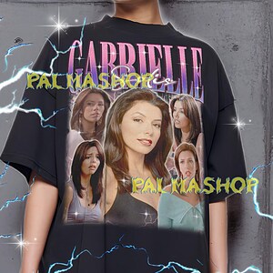 Puede incluir: Camiseta negra de gran tamaño con un gráfico de una mujer y el texto "GABRIELLE PALMASHOP". El diseño tiene una estética vintage con detalles de rayos. La modelo lleva una camiseta XL. La camiseta es fiel a la talla.