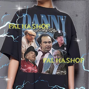 May include: Black t-shirt featuring a collage of Danny DeVito's image with the text "DANNY" and "PALMASHOP" in a stylized font. The shirt is worn by a person. The text at the bottom of the image says "The first model is wearing a XL shirt."