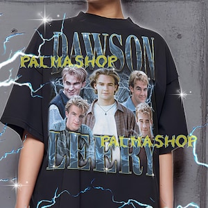 May include: Black oversized t-shirt featuring a graphic of the TV show "Dawson's Creek" cast. The shirt has the text "DAWSON" and "LEERY" in a distressed font, with "PALMASHOP" above and below. The shirt is worn by a person.