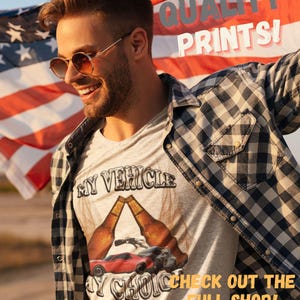 May include: A man wearing a grey t-shirt with a red car and two beer bottles printed on it. The text on the shirt reads "My Vehicle My Choice". The man is holding an American flag behind him. The text "Quality Prints!" is printed on the flag. The text "Check out the full shop! Hilarious tees for any occasion." is printed below the man.