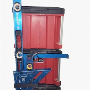 May include: A stack of red toolboxes with a blue level and angle measuring tools. The level is marked "Empire" and has bubble vials. The angle measuring tools are also blue and have measurement markings. The toolboxes are stacked on a black base.