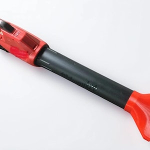 May include: A red and black handheld tool with a nozzle. The tool has a red handle and a black cylindrical body. The nozzle is a bright red, flat, and rectangular shape. The tool is designed for a specific task, likely related to cleaning or maintenance.