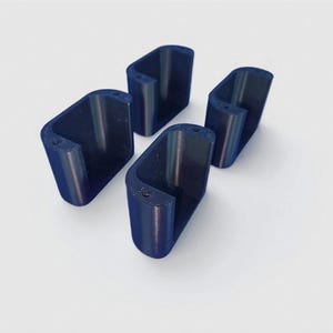 May include: Four dark blue, U-shaped, 3D-printed objects are arranged on a white surface. Each object has a rectangular base and a curved top, with a small hole near the top. The objects are evenly spaced.