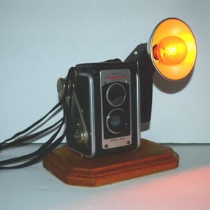Table Lamp Night Light ~ Repurposed Upcycled Duaflex III Camera Lamp on wood base w-Orange globe  bulb. Camera is mounted on a wood base.