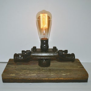 May include: A steampunk-style table lamp made from repurposed industrial pipe fittings. The lamp features a vintage Edison bulb and a rustic wooden base.