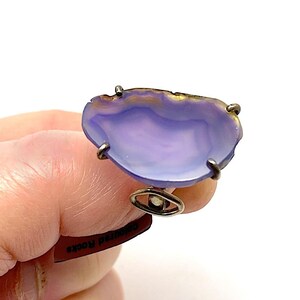 May include: A silver ring with a large, purple agate stone set in the center. The stone has a natural, irregular shape and a smooth, polished surface.
