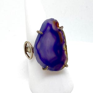 May include: A silver ring with a large purple agate stone. The stone has a natural, irregular shape and is set in a simple silver band.