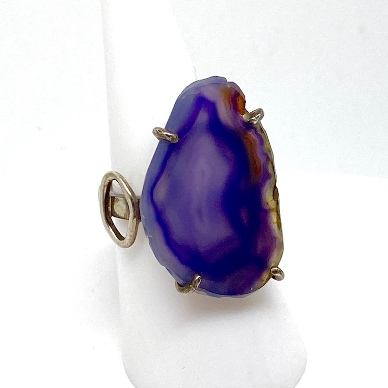 May include: A silver ring with a large purple agate stone. The stone has a natural, irregular shape and is set in a simple silver band.