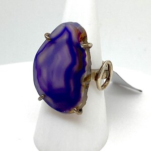 May include: A silver ring with a large, purple agate stone set in the center. The stone has a unique, swirling pattern and is surrounded by silver prongs.