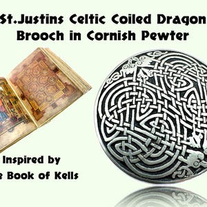 May include: A Celtic coiled dragon brooch in Cornish pewter, inspired by the Book of Kells. The image shows the brooch next to an open book with illuminated manuscript pages. The brooch has a detailed, interwoven design.