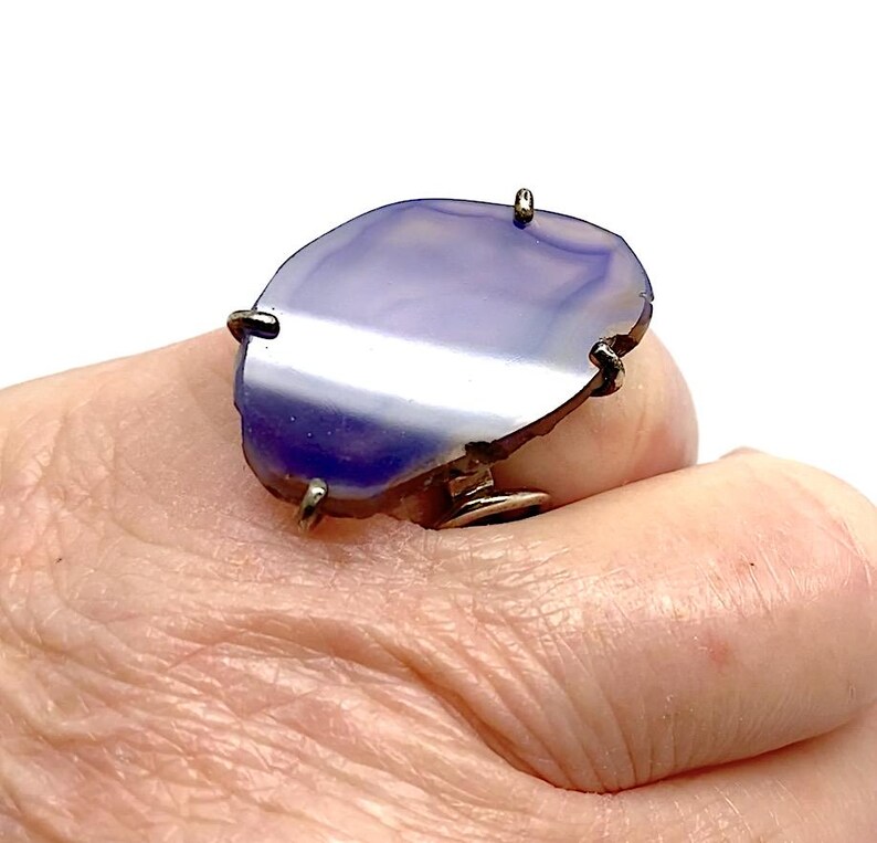 May include: A silver ring with a large, oval-shaped purple agate stone. The stone has a natural, irregular edge and a white band running through the center.