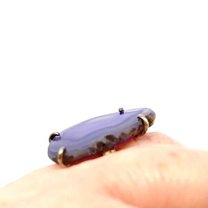 May include: A purple agate ring with a silver setting. The ring is on a finger.