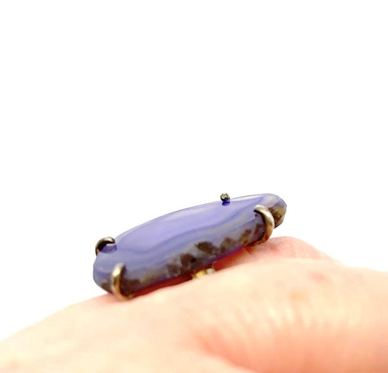 May include: A purple agate ring with a silver setting. The ring is on a finger.