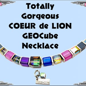 Op de afbeelding: Een kleurrijke ketting met vierkante, geometrische kralen in roze, paarse, blauwe en iriserende tinten. De ketting heeft een zilverkleurige sluiting en een kleine bedel met "COEUR-LION". De tekst "Totally Gorgeous COEUR de LION GEOcube Necklace" wordt weergegeven.