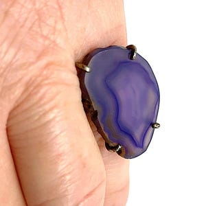 May include: A purple agate ring with silver settings. The ring is set on a finger.