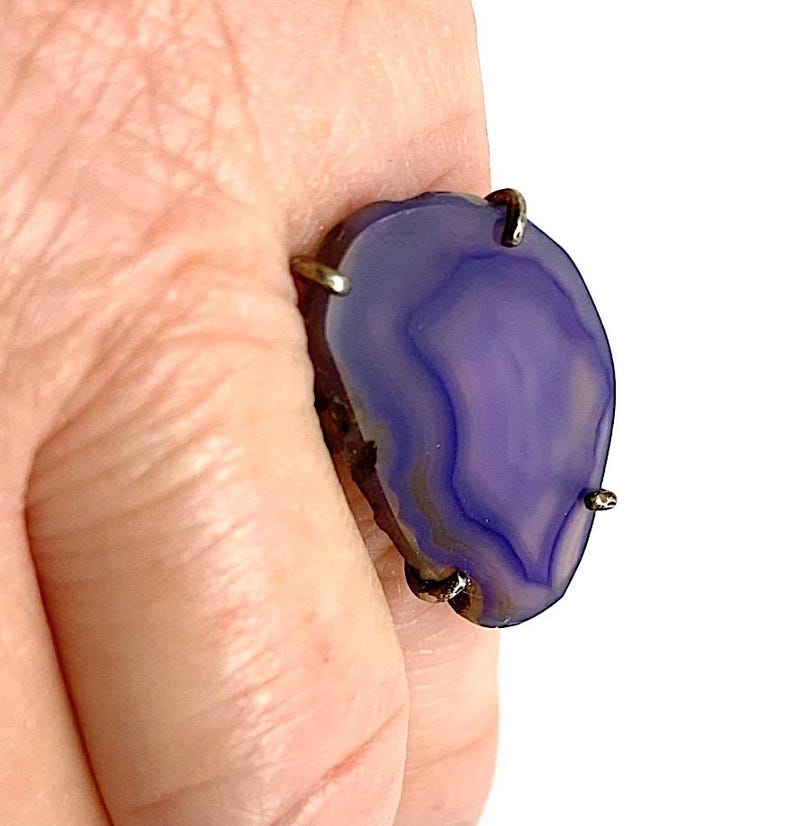 May include: A purple agate ring with silver settings. The ring is set on a finger.