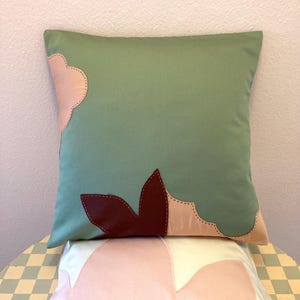 Pode incluir: Duas almofadas decorativas com um design floral verde, rosa e marrom. As almofadas estão empilhadas uma em cima da outra.