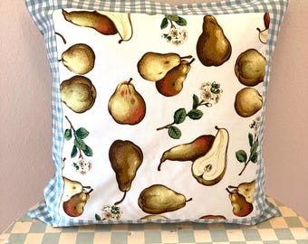 Op de afbeelding: Vierkant decoratief kussen met een witte achtergrond met een patroon van bruine en rode peren en takjes witte bloemen. Het heeft een lichtblauwe en witte ruitjesrand.