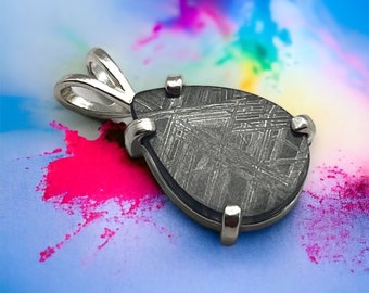 May include: A silver pendant featuring a teardrop-shaped piece of meteorite with a Widmanstätten pattern. The pendant is set in a silver bezel and has a silver bail.