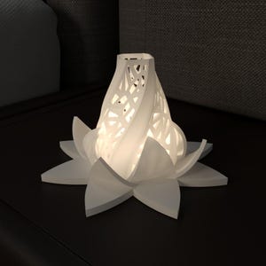 Peut inclure: Une lampe blanche en impression 3D en forme de fleur de lotus avec un motif géométrique. La lampe est allumée et diffuse une lueur chaude.