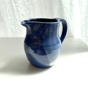 Peut inclure: Un pichet en céramique fait main avec une glaçure bleu profond brillante et un corps lisse et arrondi. Le récipient présente une anse incurvée sur le côté droit et un petit bec verseur intégré au bord supérieur, affichant une couleur unie.