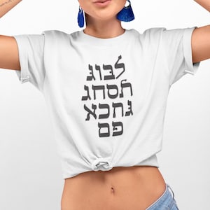May include: White t-shirt with black Hebrew text that reads "עצבו חסתה אהבה כס"
