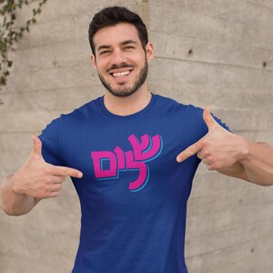 May include: A royal blue t-shirt with a pink and blue graphic of the Hebrew word "Shalom" in a modern font.