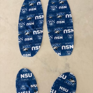 May include: Four blue fabric cutouts with the text "NSU Florida" in white. Two are elongated, resembling bunny ears, and two are oval-shaped. The fabric has a repeating pattern of the text and a shark graphic.