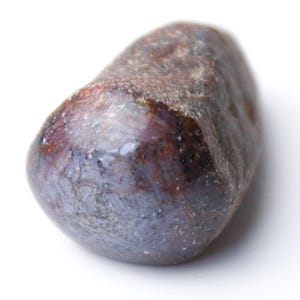 May include: A polished, oval-shaped gemstone with a mix of dark brown and purplish-blue hues. The stone has a smooth, glossy surface and appears to be naturally formed. The gemstone is set against a plain white background.