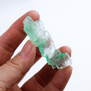 Peut inclure: Un amas de cristaux de sel vert, ressemblant à une petite tour, est tenu dans une main.
