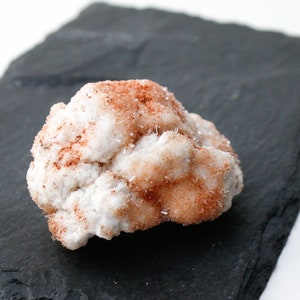 May include: A cluster of white and orange crystals with a rough, textured surface. The crystals are arranged in a random, organic pattern.