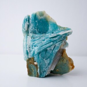 May include: A striking, raw amazonite gemstone with a vibrant turquoise hue. The stone features a layered, textured surface with areas of white, brown, and green. This natural crystal is a unique piece for collectors or those interested in minerals.