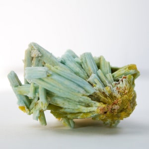 May include: A cluster of blue-green and yellow crystals. The crystals are long and thin, and they are arranged in a random pattern.