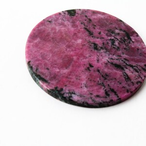 May include: A round, pink and black, polished, natural stone coaster.