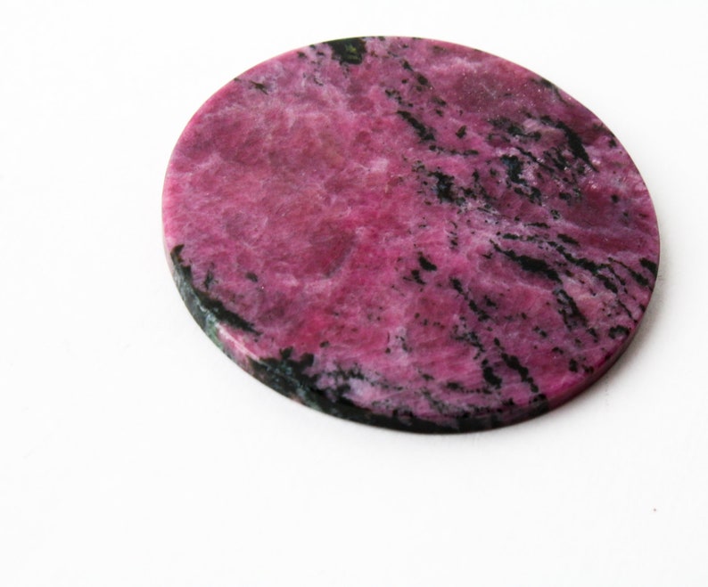 May include: A round, pink and black, polished, natural stone coaster.