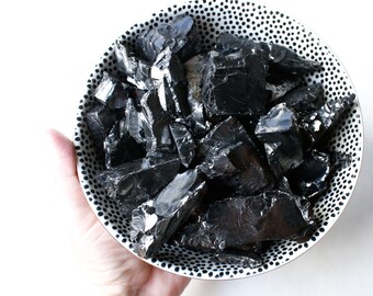 May include: A bowl filled with black obsidian crystals. The bowl has a white background with black polka dots.