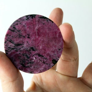 May include: A round, pink and black, polished, natural stone with a marbled pattern.
