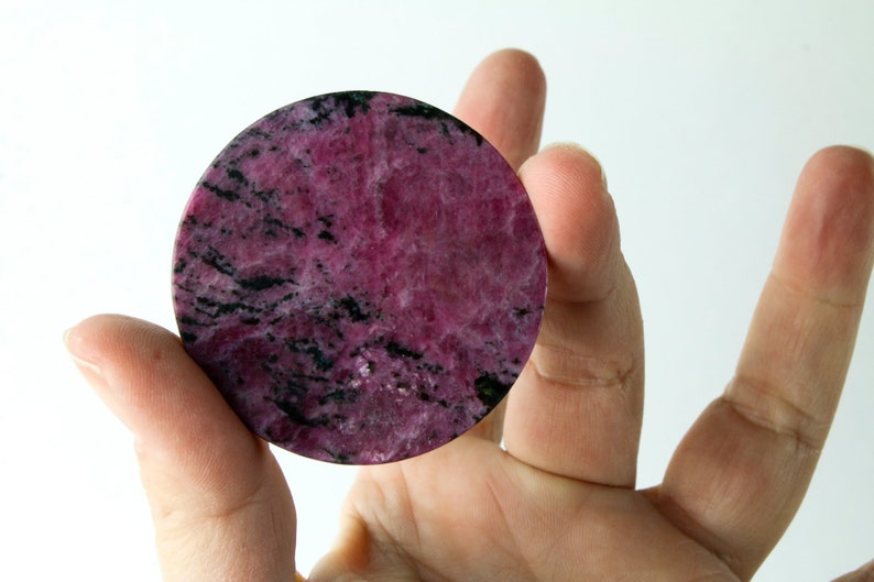 May include: A round, pink and black, polished, natural stone with a marbled pattern.