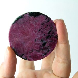 May include: A round, polished pink and black gemstone with a swirling pattern.