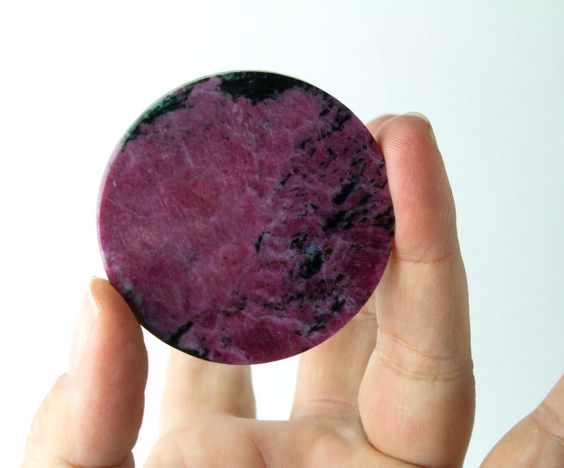 May include: A round, polished pink and black gemstone with a swirling pattern.
